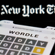 A phone user holds an iPhone with Wordle on it in front of the New York Times logo.